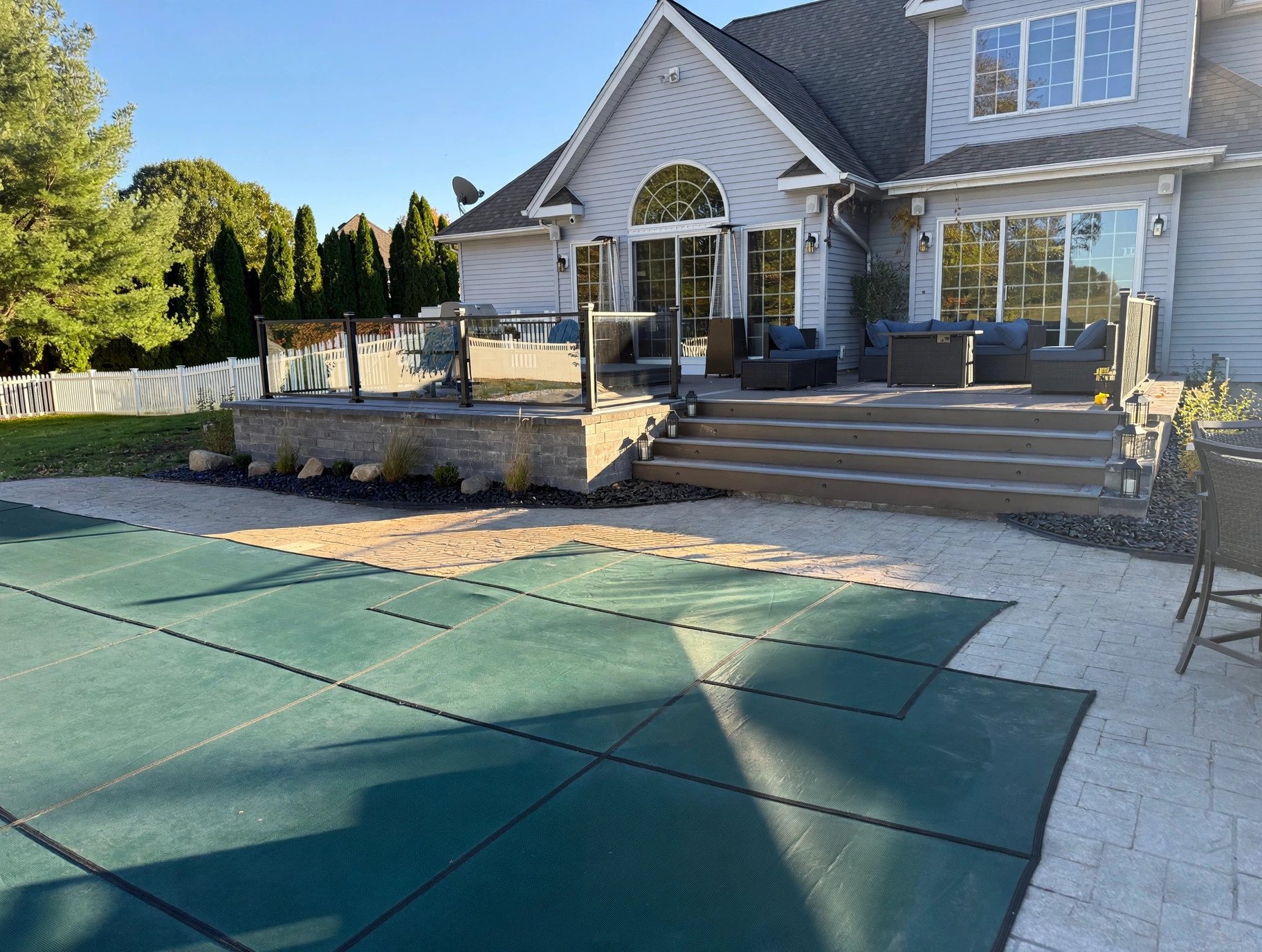 Ground-up custom deck in Suffield, Connecticut with glass panel railing, real stone skirting, wide entry stairs and an in-ground pool